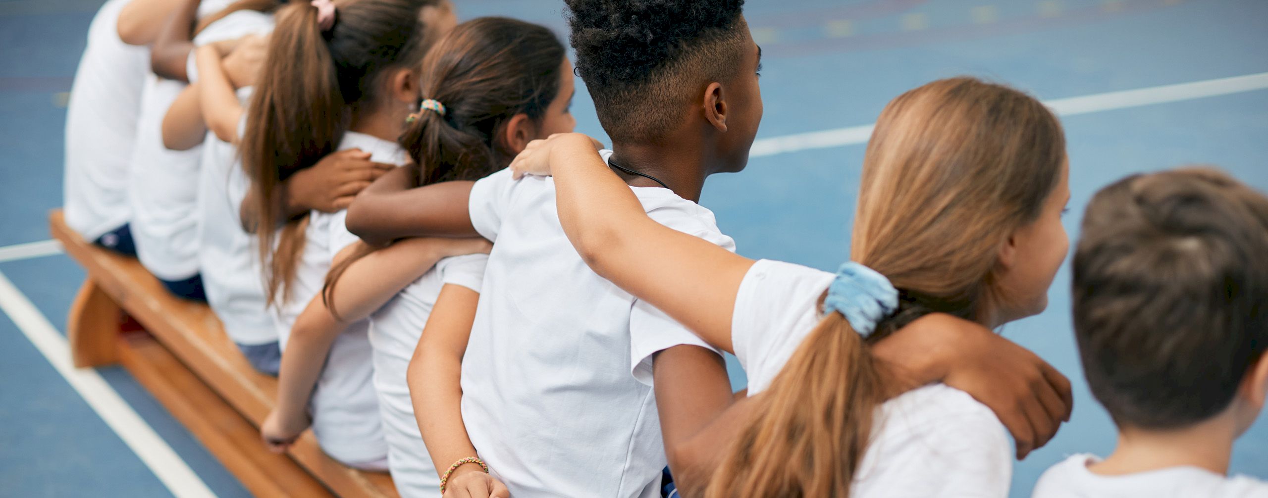 Kinder sitzen auf einer Bank und legen sich gegenseitig die Arme um die Schultern.