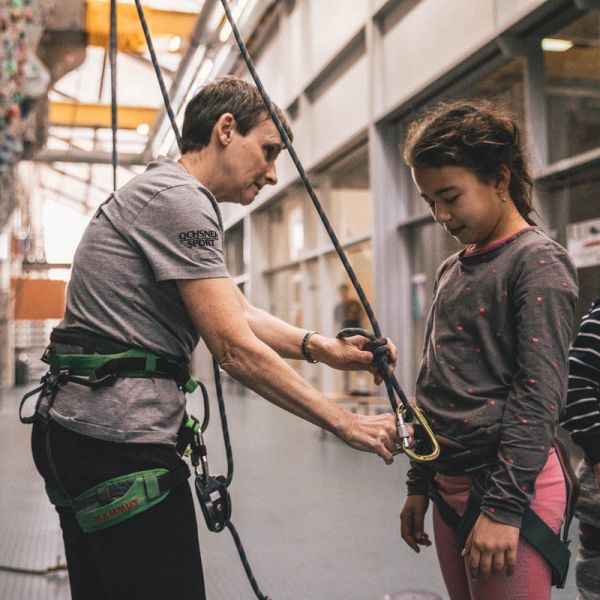 Trainerin mit Mädchen legt Klettergeschirr an 