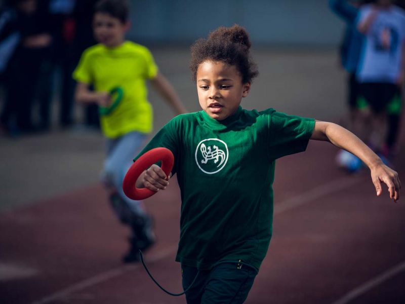junge frau beim Staffellauf mit rotem Ring in der Hand und grünes Trikot