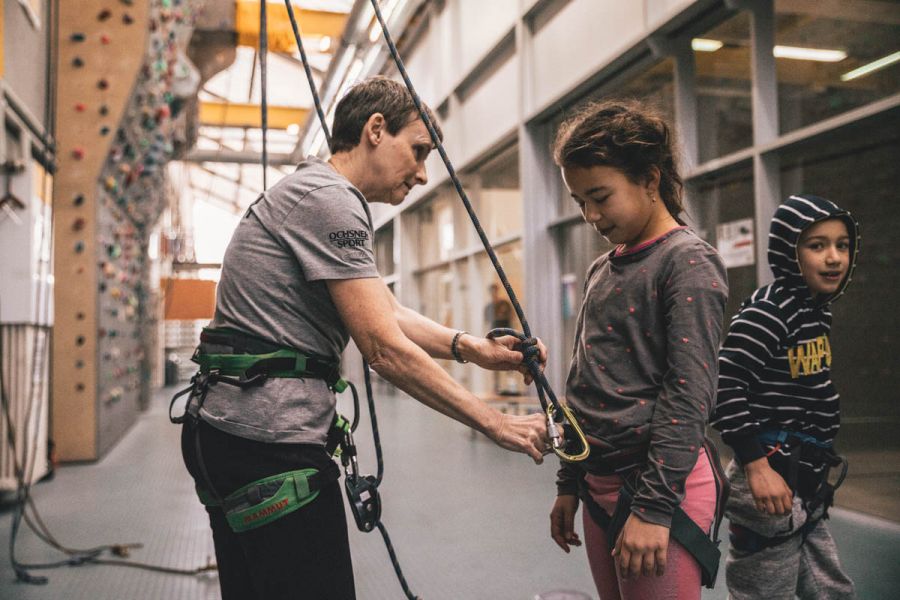 Klettertrainerin legt jungen Mädechen Klettergeschirr um